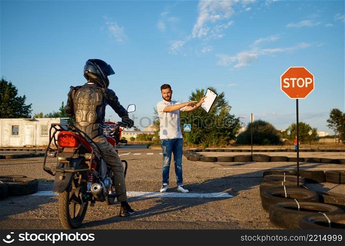 Male student in helmet and instructor, skill test on motordrome in motorcycle school. Training of motorcyclists beginners, biker practicing in motorschool. Male student and instructor, test on motordrome