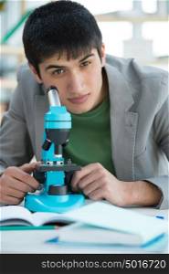 Male student in laboratory looking at camera while working with microscope and making notes