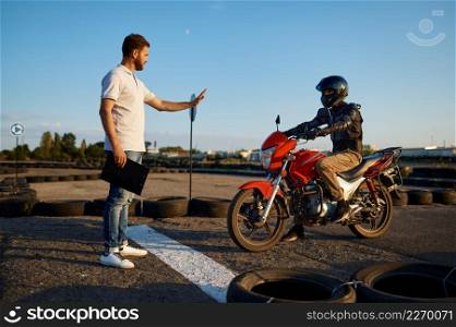 Male student on motorbike and instructor at the starting line, lesson on motordrome in motorcycle school. Training of motorcyclists beginners, biker practicing in motorschool. Student at the starting line, motorcycle school