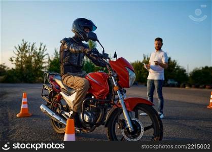 Male student on motorbike and instructor, riding between the cones, lesson in motorcycle school. Training of motorcyclists beginners, biker practicing on motordrome. Riding between cones, lesson in motorcycle school