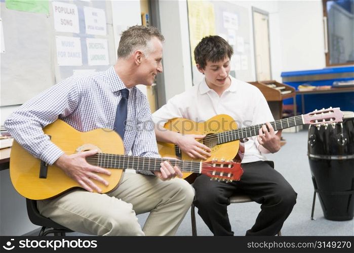 Male student receiving guitar lesson from teacher in classroom