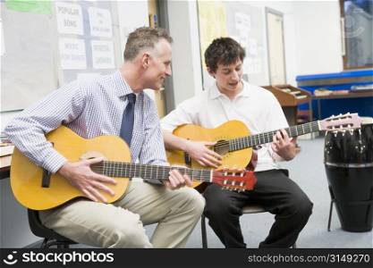 Male student receiving guitar lesson from teacher in classroom