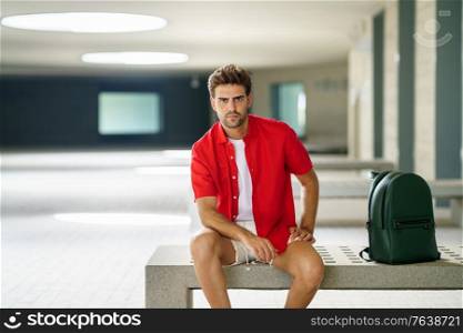 Male student sitting on a college campus bench. Young man in urban background.. Male student sitting on a college campus bench