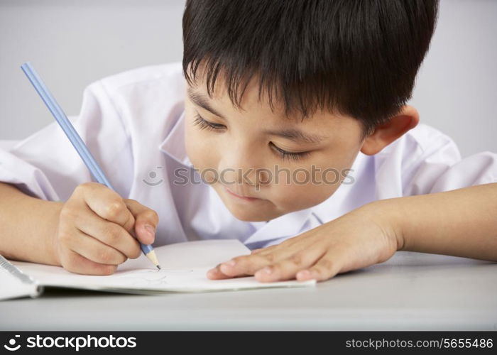 Male Student Working At Desk In Chinese School Classroom