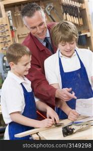 Male students reviewing woodworking plans with teacher