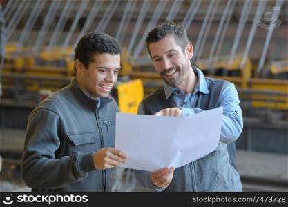 male supervisor with worker discussing over blueprints in industry