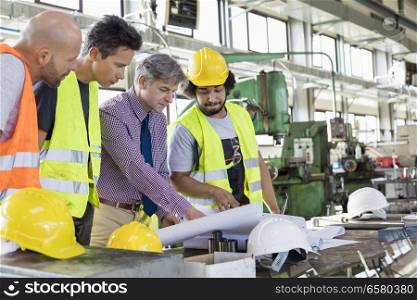 Male supervisor with workers discussing over blueprints in industry