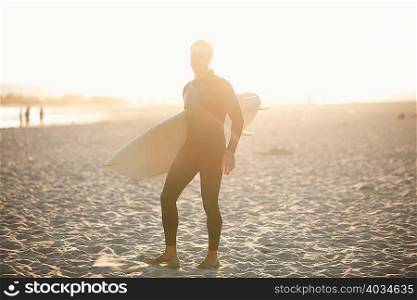 Male surfer carrying surfboard on sunlit Venice Beach, California, USA
