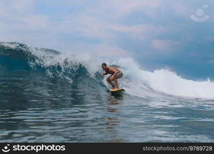 Male surfer on a blue wave at Bali island