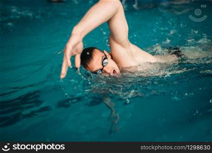Male swimmer in goggles swims on workout in swimming pool. Aqua sport training, healthy lifestyle. Male swimmer swims on workout in swimming pool