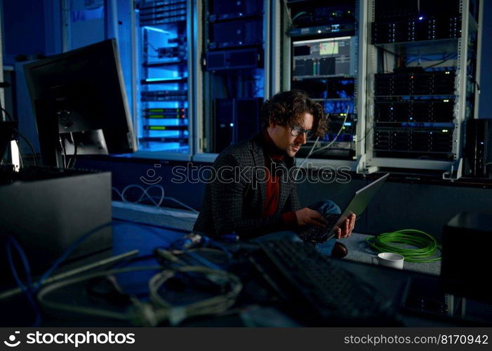 Male system administrator working in server room using laptop while inspecting in computer. Database management and maintenance concept. Male system administrator working in server room using laptop