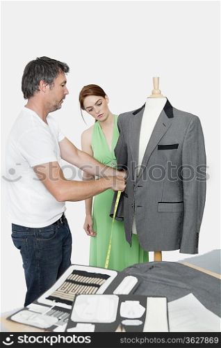 Male tailor taking measurement of suit while female coworker standing besides