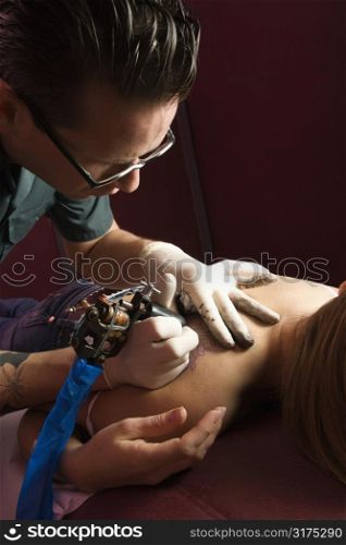 Male tattoo artist tattooing Caucasian woman.