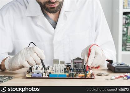 male technician checking computer with digital multimeter wooden desk