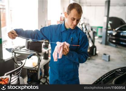 Male technician checks car engine oil level with dipstick. Auto-service, vehicle maintenance, repairman with tools. Male technician works with car engine