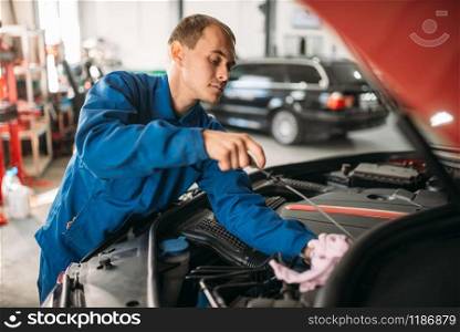 Male technician checks car engine oil level with dipstick. Auto-service, vehicle maintenance, repairman. Male technician works with car engine
