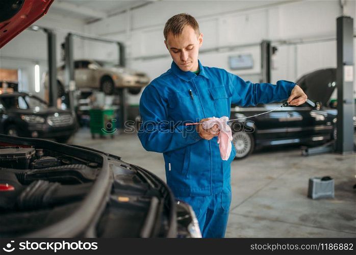 Male technician checks car engine oil level with dipstick. Auto-service, vehicle maintenance, repairman. Male technician works with car engine