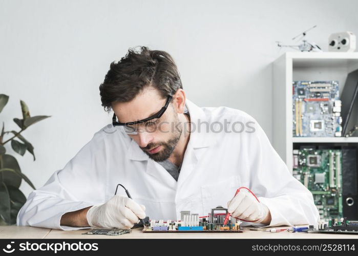 male technician examining broken computer with digital multimeter