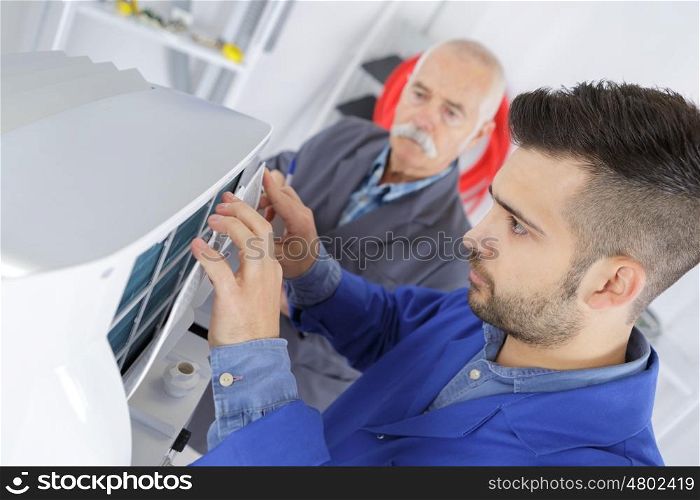 male technician is repairing a printer assited by senior