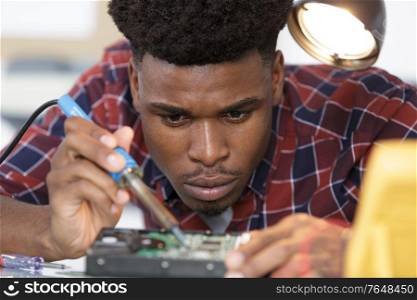 male technician using soldering iron on computer hardware
