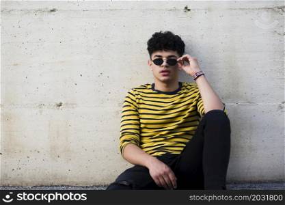 male teenager sitting ground leaning concrete wall
