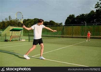 Male tennis player with racket hits the ball on outdoor court. Active healthy lifestyle, sport game competition, fitness training with racquet. Male tennis player with racket hits the ball