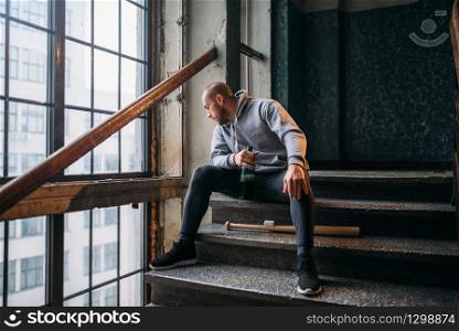 Male theif with baseball bat sits on stairs. Street robber waiting for victim. Crime concept, robbery attack danger. Male theif with baseball bat sits on stairs