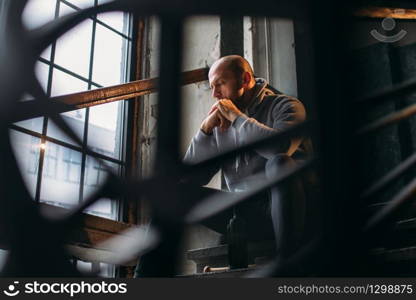 Male theif with bottle of alcohol sits on stairs. Street robber waiting for victim. Crime concept