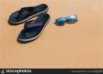 Male thongs and sunglasses lying on the sandy beach; selective focus