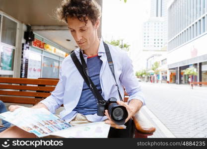 Male tourist in city. Happy male tourist in city with camera and map