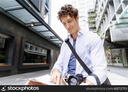 Male tourist in city. Happy male tourist in city with camera and map