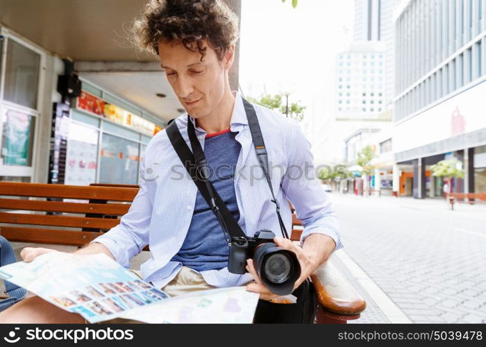 Male tourist in city. Happy male tourist in city with camera and map