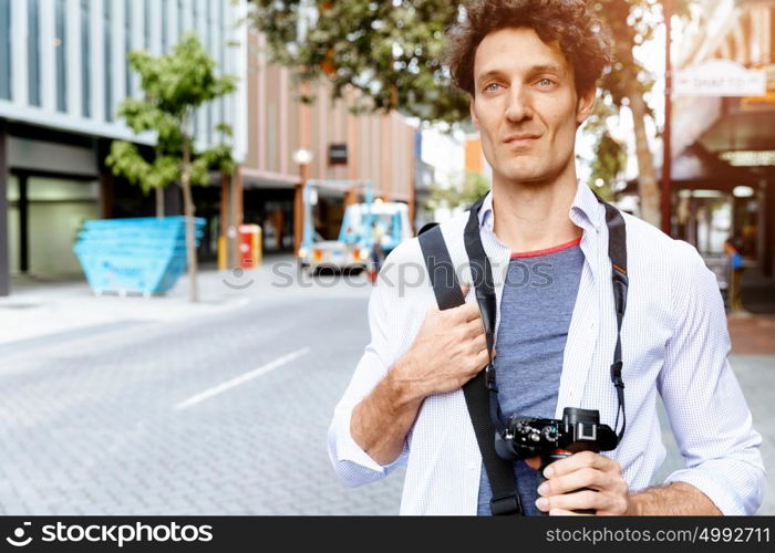 Male tourist in city. Happy male tourist walking in city with camera