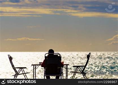 Male tourist person sitting on beach seashore at sunset, relaxing and enjoying scenic sea view. Summer holidays.. Male person enjoy sea view at sunset