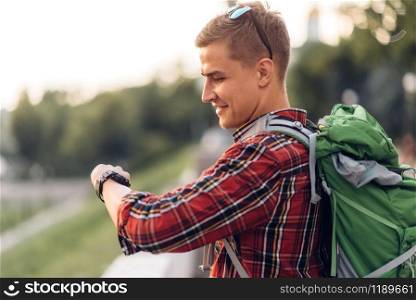 Male tourist with backpack looking at the clock, excursion in town. Summer hiking. Hike adventure of young man