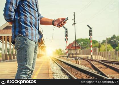 Male tourists are carrying a smartphone headphone jack. Standing near the train tracks, vintage tone.