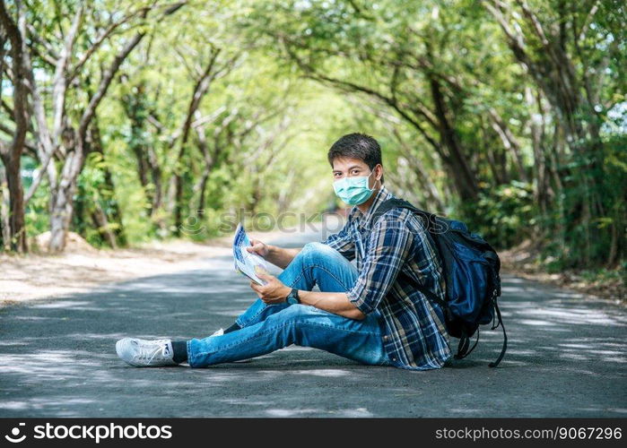 Male tourists sit and look at the map on the road.