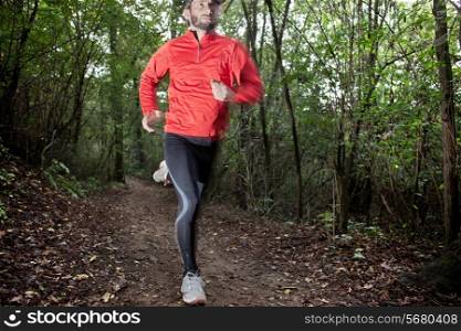 Male trail runner running in the forest on a trail. Red shirt and black pants. Summer season. Slight blur in runner to show motion. Horizontal composition.. Cross country running