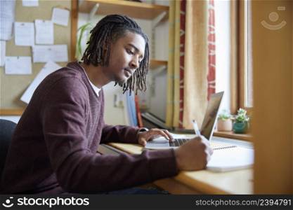 Male University Or College Student Studying With Laptop At Desk In Room