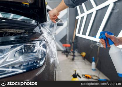 Male worker applies car protection film on front fender. Installation of coating that protects the paint of automobile from scratches. New vehicle in garage, tuning. Worker applies car protection film on front fender