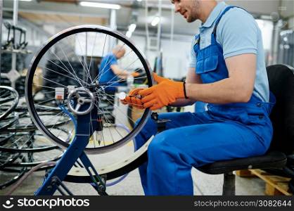 Male worker at the machine tool checks bicycle rim on factory. Bike wheels assembly in workshop, cycle parts installation. Male worker at the machine tool checks bicycle rim