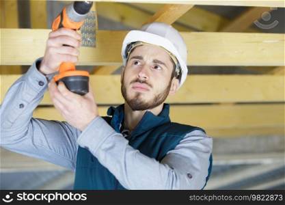 male worker drills roof of a wooden frame