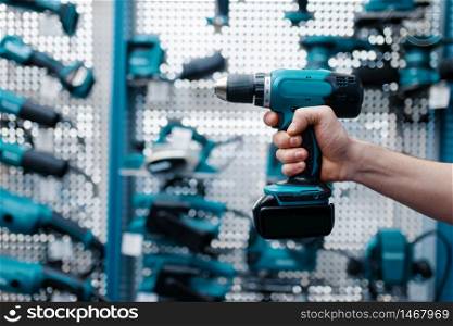 Male worker hand holds electric drill in tool store. Choice of professional equipment in hardware shop, electrical instrument supermarket. Male worker hand holds electric drill, tool store