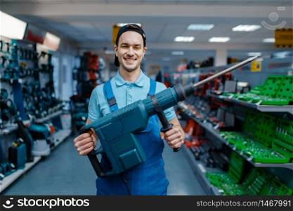 Male worker holds big electric perforator in tool store. Choice of professional equipment in hardware shop, electrical instrument supermarket. Worker holds big electric perforator in tool store