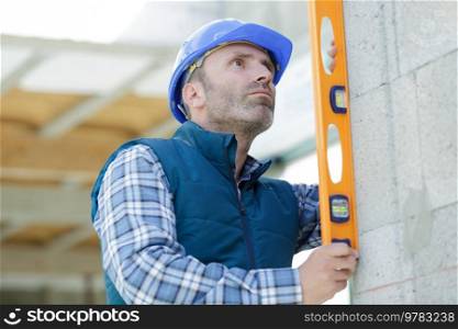 male worker in helmet is measuring wall with level
