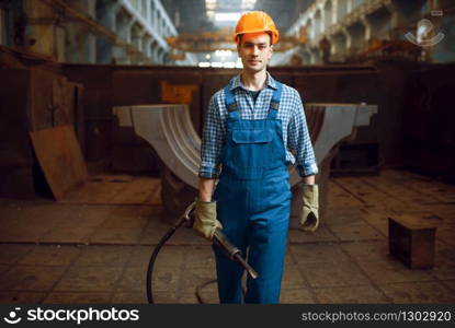 Male worker in uniform and helmet holds pneumatic jackhammer on factory. Metalworking industry, industrial manufacturing of steel products. Male worker holds pneumatic jackhammer on factory