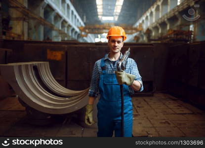 Male worker in uniform and helmet holds pneumatic jackhammer on factory. Metalworking industry, industrial manufacturing of steel products. Male worker holds pneumatic jackhammer on factory