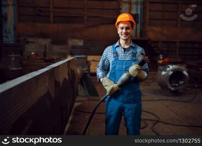 Male worker in uniform and helmet works with metal workpieces on factory. Metalworking industry, industrial manufacturing of steel products. Worker in helmet works with metal workpieces