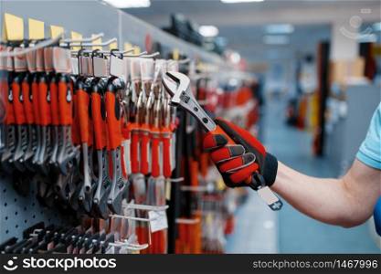 Male worker in uniform choosing adjustable wrench in tool store. Choice of professional equipment in hardware shop, instrument supermarket. Worker choosing adjustable wrench in tool store