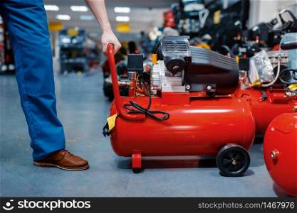 Male worker in uniform choosing pneumatic compressor in tool store. Choice of professional equipment in hardware shop, instrument supermarket. Worker choosing pneumatic compressor in tool store